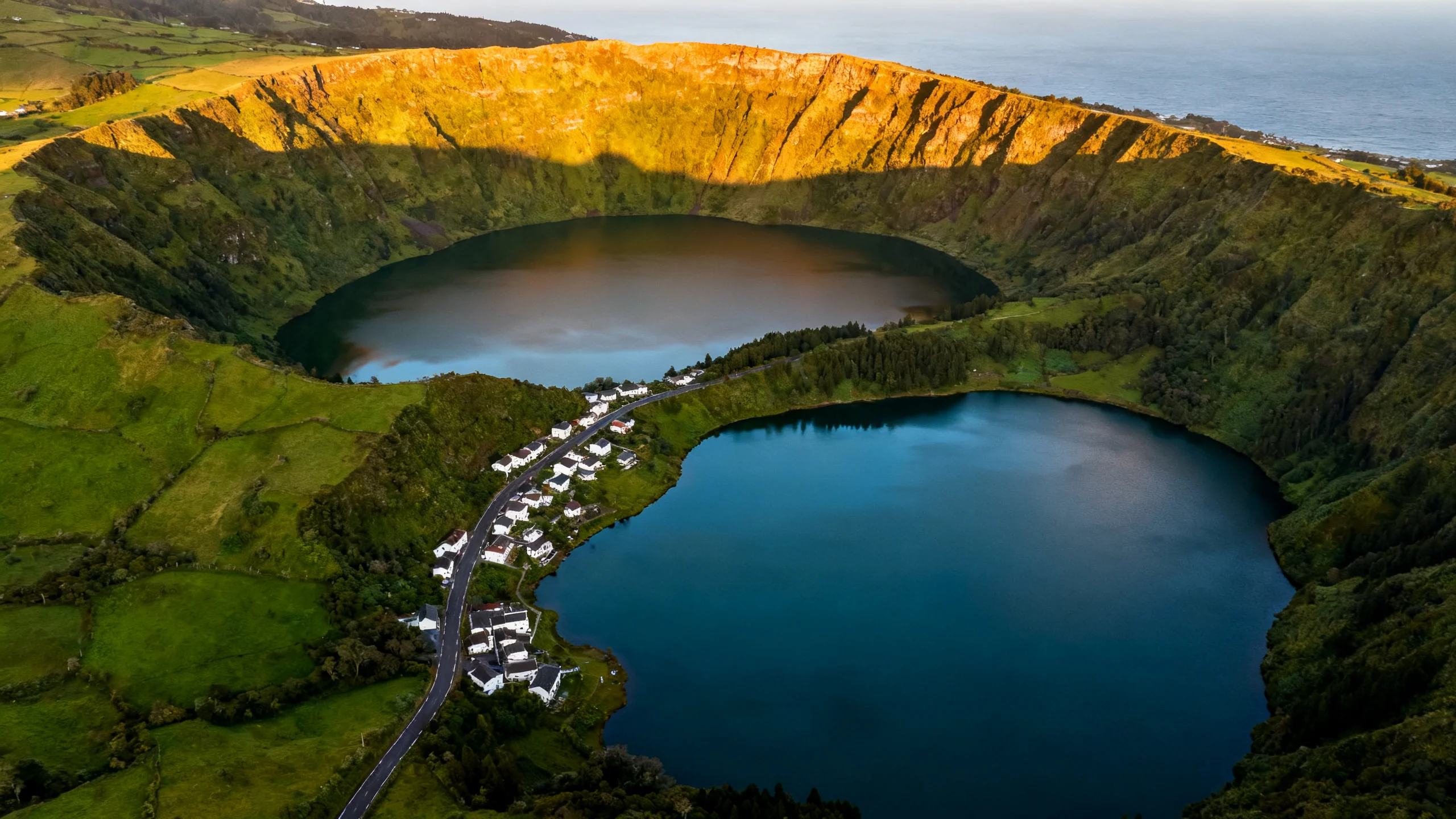 Aerial view of the twin lakes of Sete Cidades on São Miguel, Azores, with the green and blue lakes joined by a narrow strip of land, the small village of Sete Cidades on the lake shore, and the towering crater rim covered in green vegetation, late afternoon golden light hitting the western rim